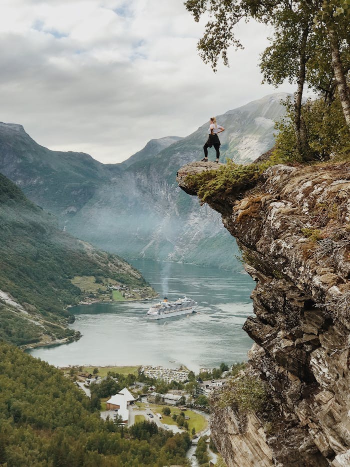Crafting Captivating Headlines: Your awesome post title goes here Person enjoys breathtaking view from a cliff above Geiranger Fjord, Norway, with clear skies and cruise ship below.