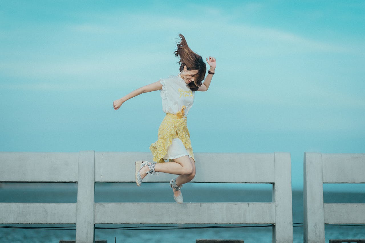 Mastering the First Impression: Your intriguing post title goes here Woman jumping cheerfully on a bridge under a sunny blue sky, embodying freedom and happiness.